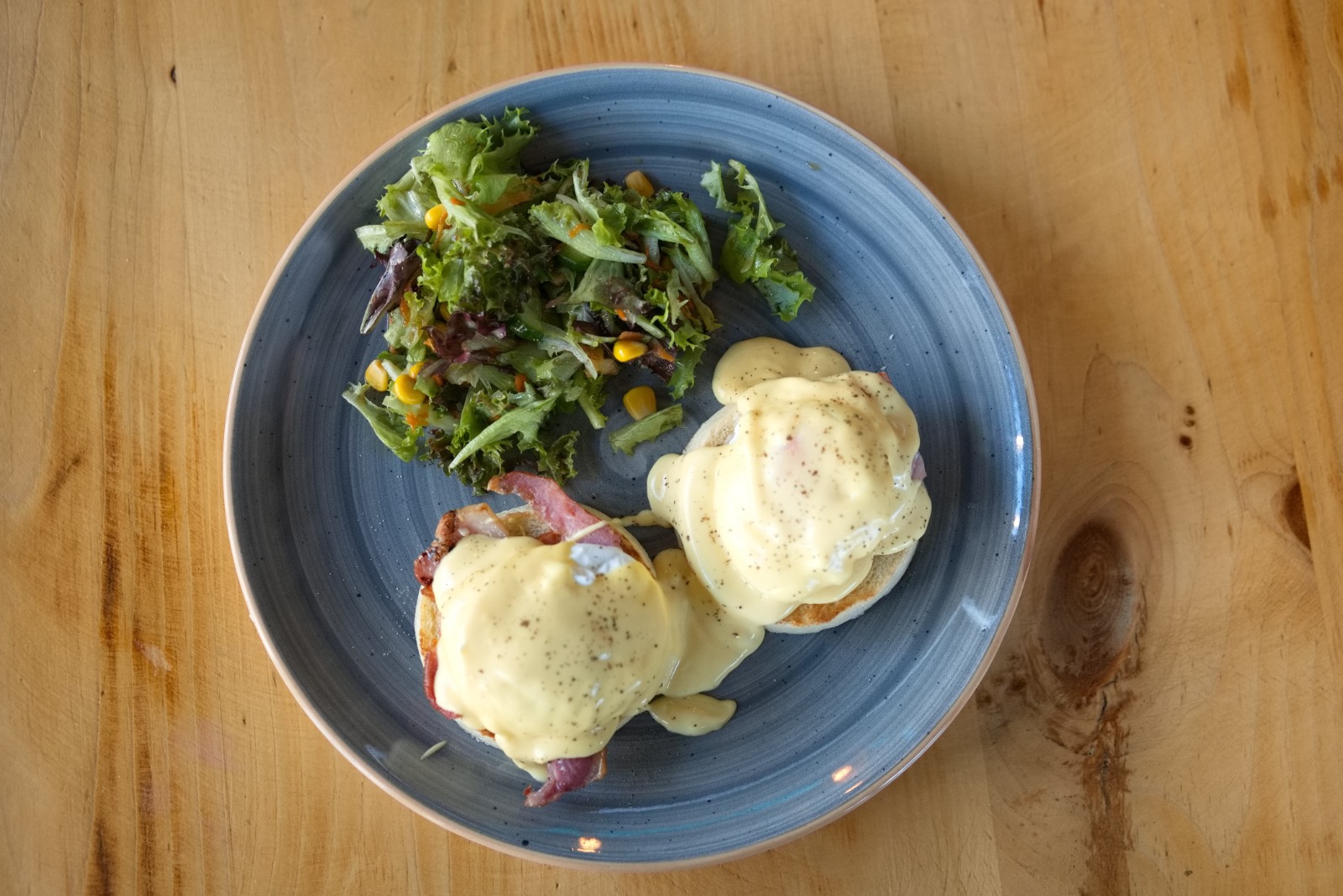 Eggs Benedict on a blue plate with side salad