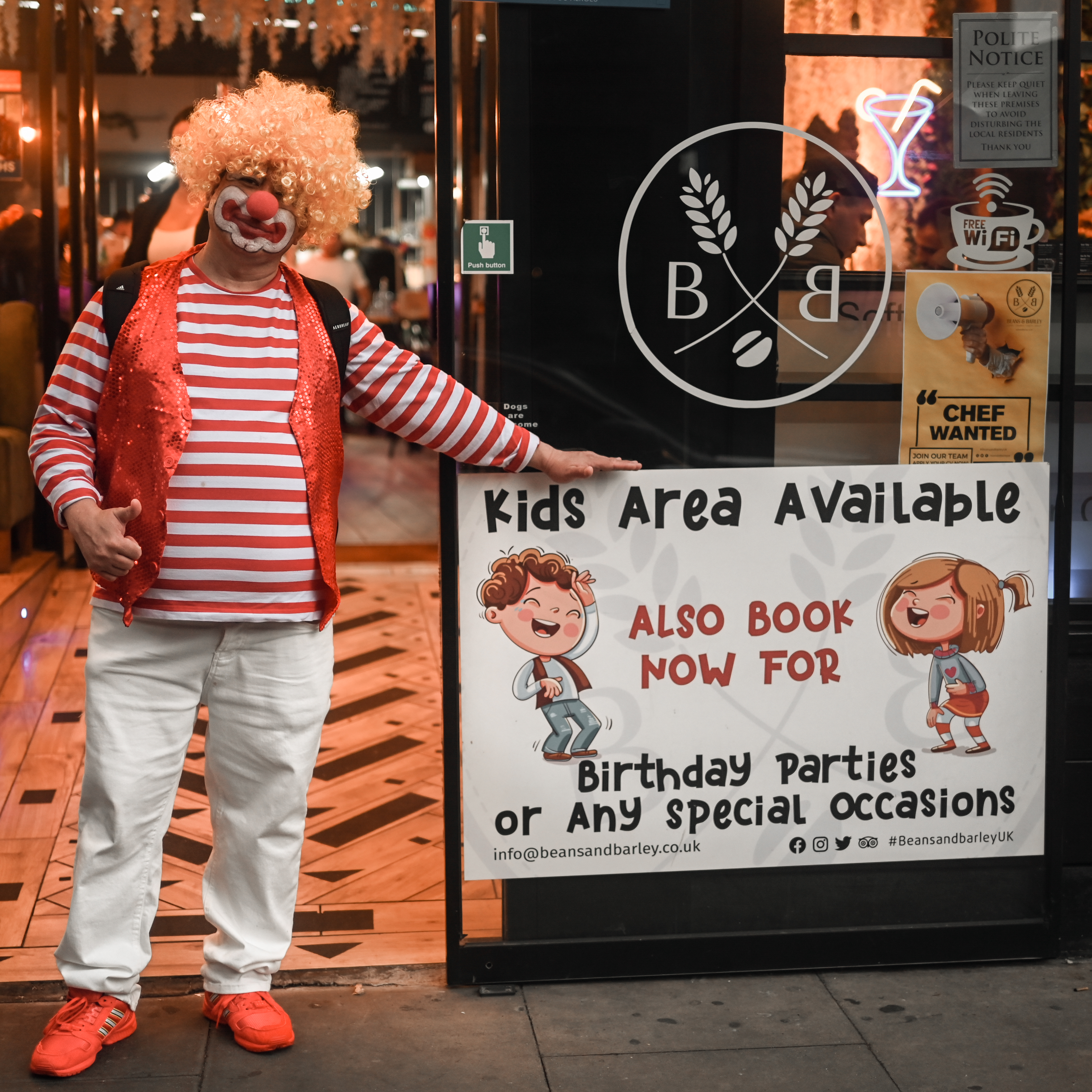 Birthday clown beside the Kids Area sign at the entrance
